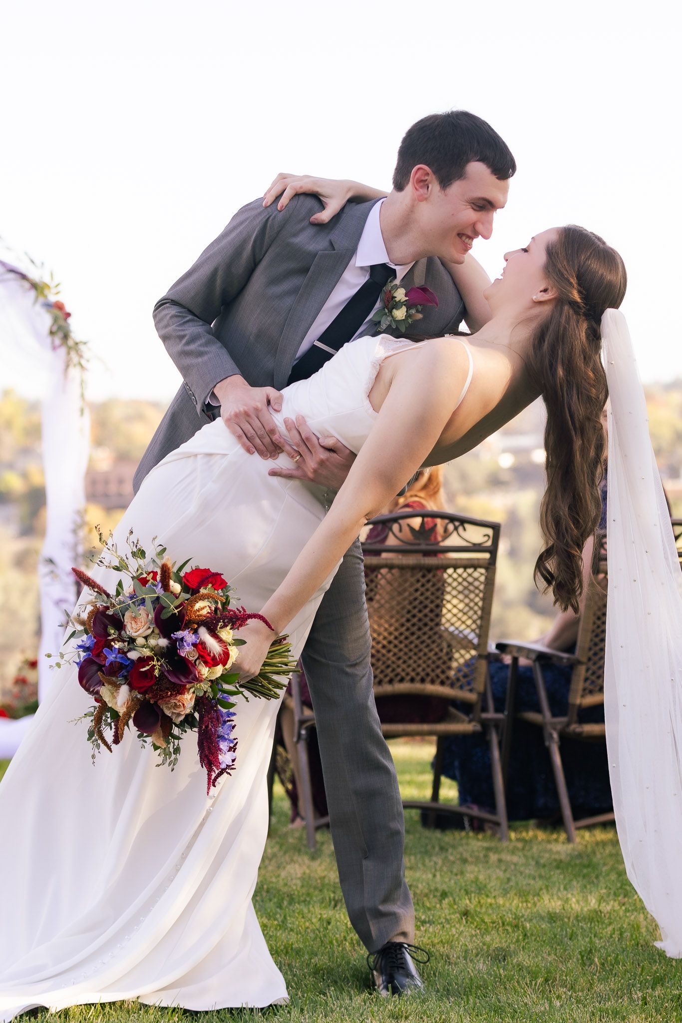 A romantic dip pose between newlyweds with the bride holding a colorful bouquet at an outdoor wedding.