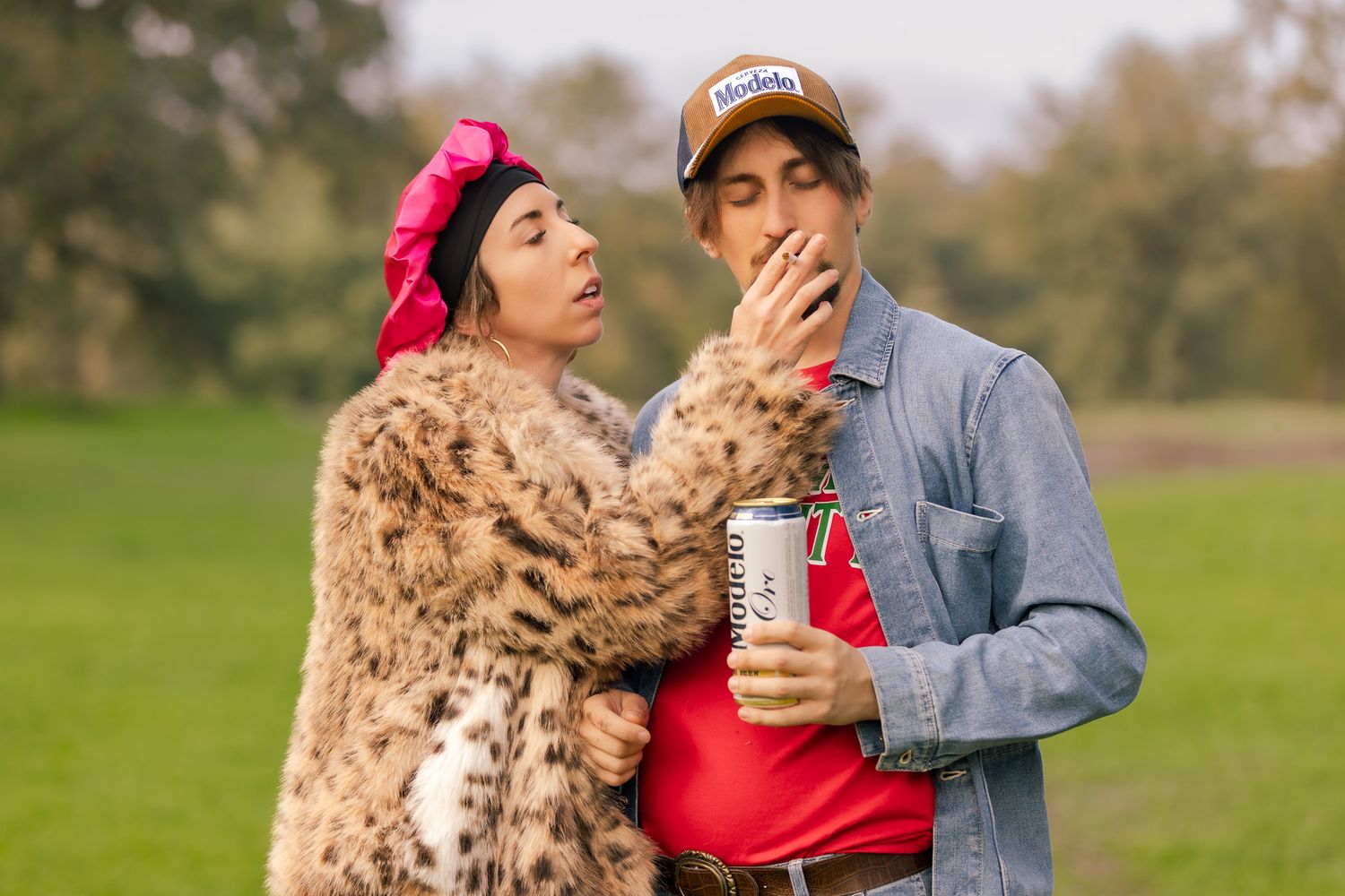 A person in a denim jacket plays with a fluffy brown goldendoodle dog in a grassy outdoor setting.