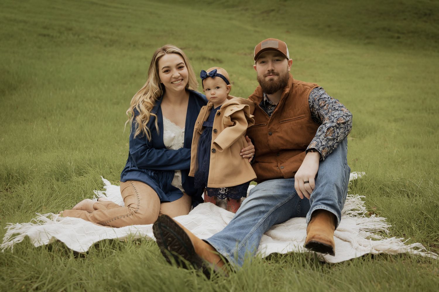 Couple relaxes on picnic blanket in grassy field during outdoor photo session.
