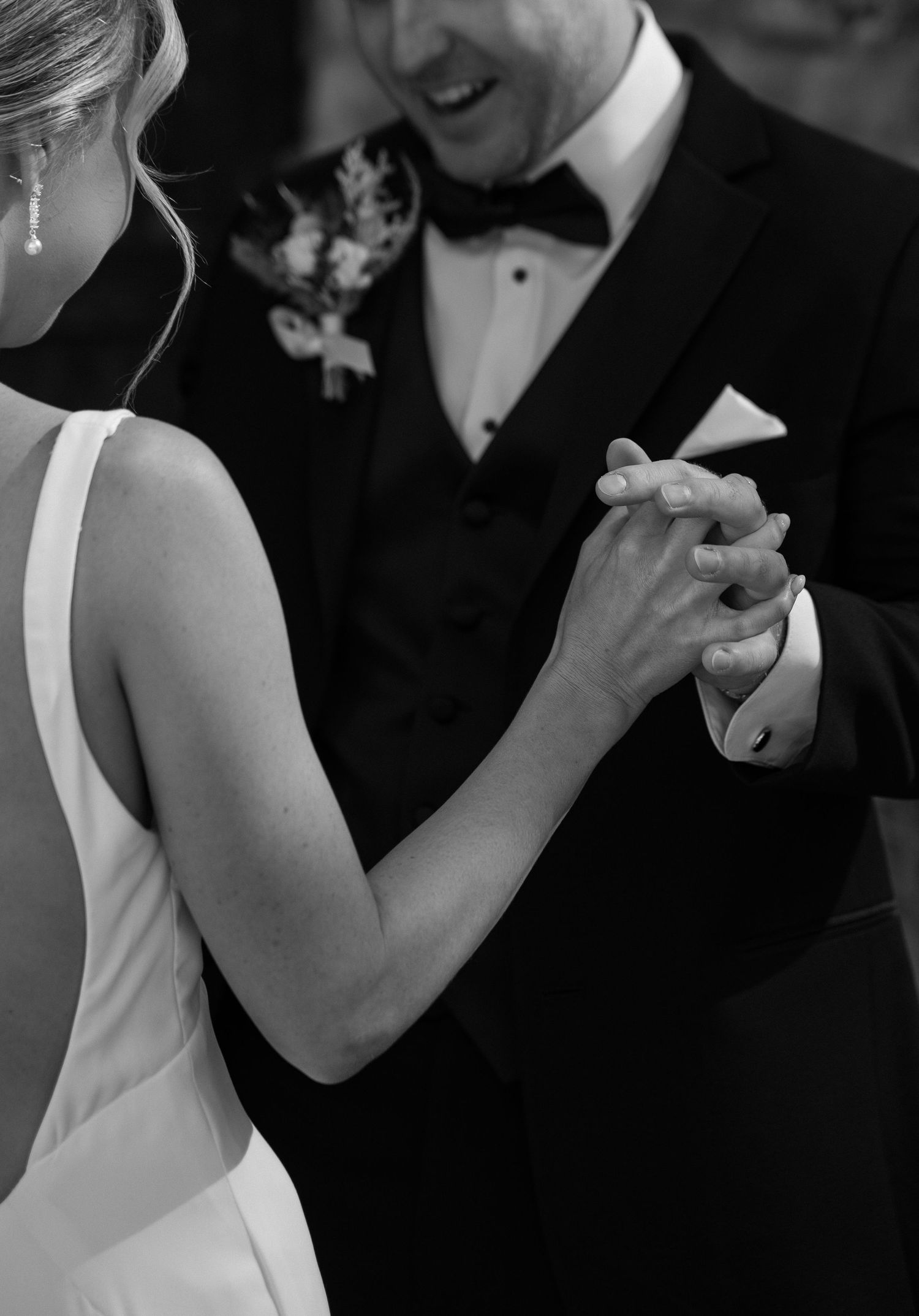 Black and white photo of a bride and groom holding hands during their first dance at a wedding reception.