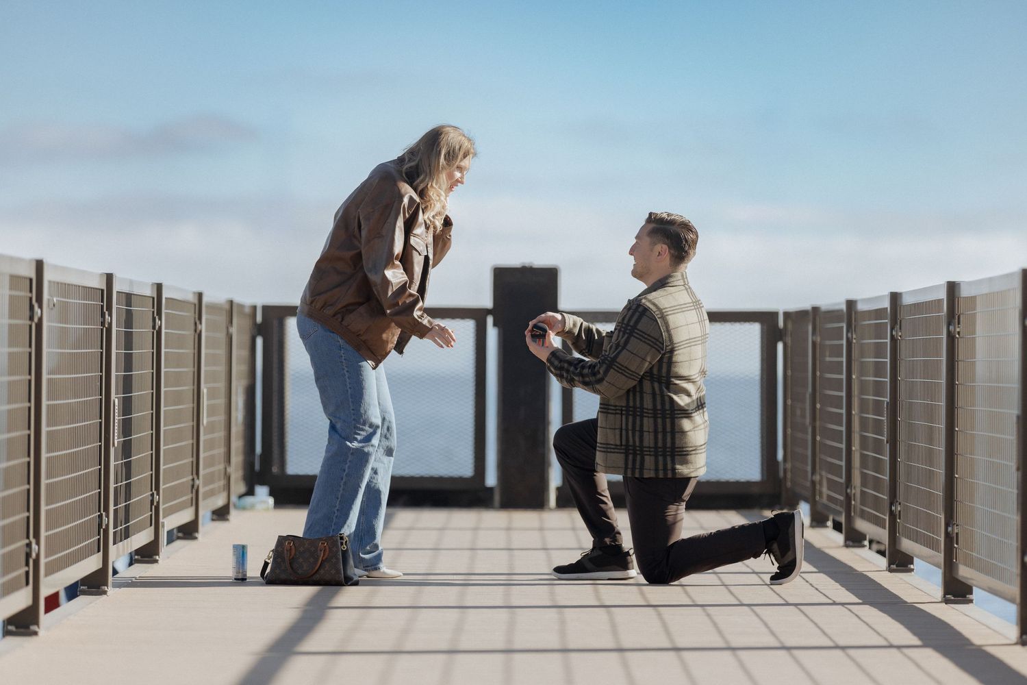 A series of photos showing a proposal moment on a wooden boardwalk overlooking the ocean on a sunny day.