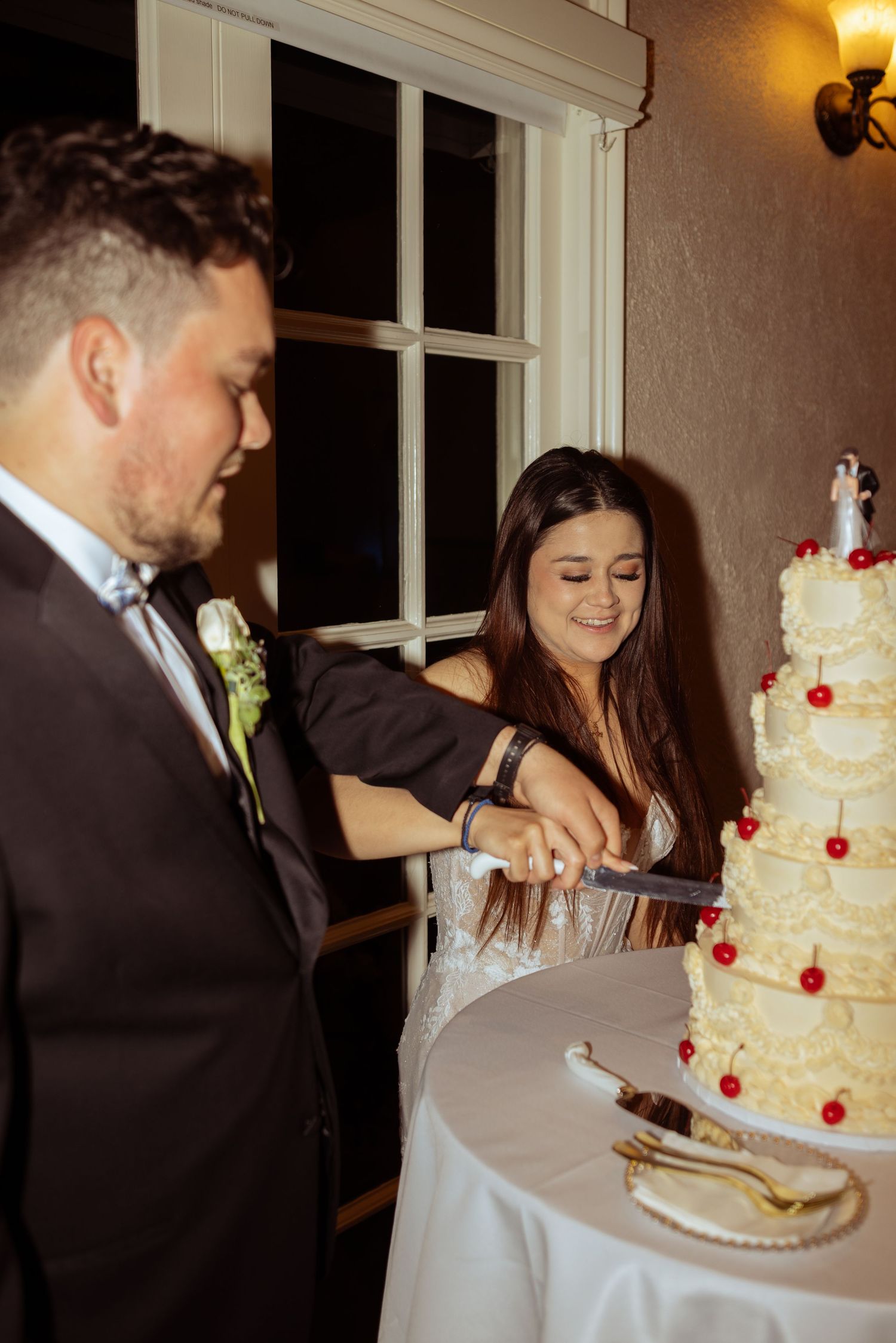 Bride and groom cutting their white wedding cake decorated with red cherries at their wedding reception.