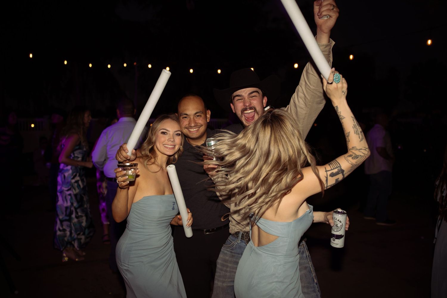 Wedding guests celebrate on the dance floor holding glow sticks during a lively outdoor evening reception.
