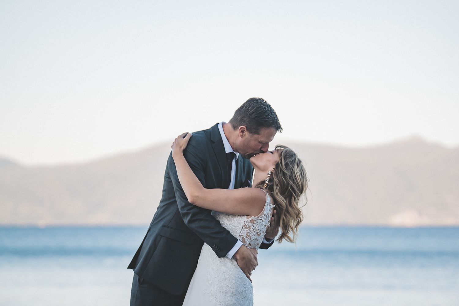 Romantic beachside wedding portraits with mountains in the background at sunset.