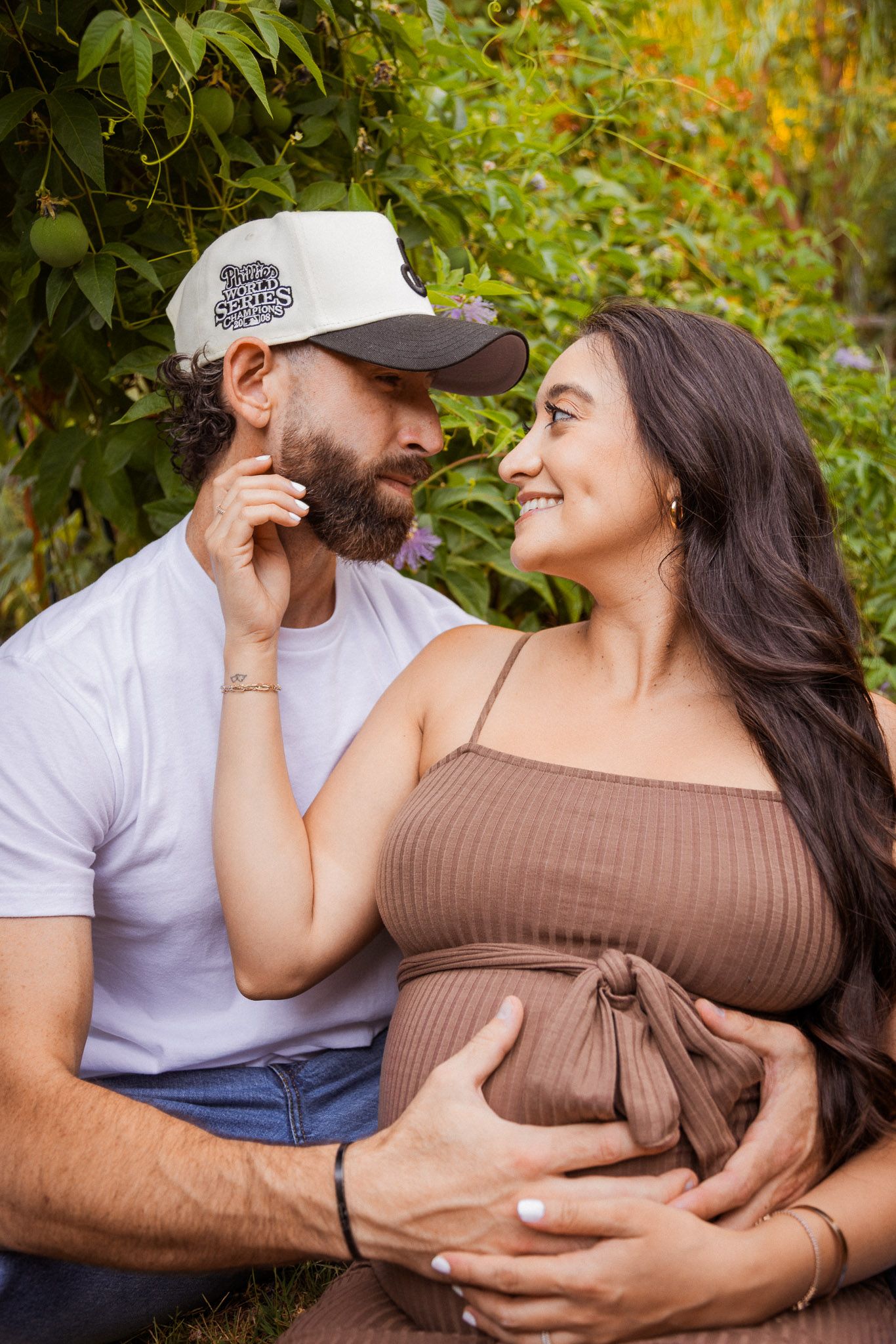 A couple embraces tenderly outdoors against a backdrop of green foliage.