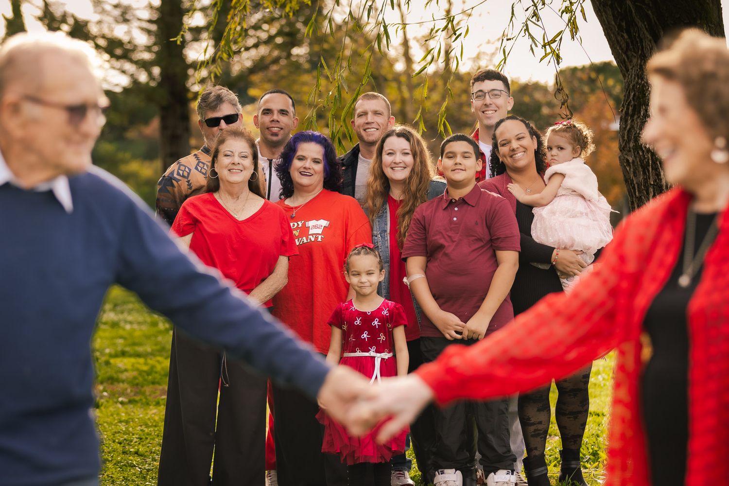 Group of people standing in a circle holding hands outdoors during a sunset gathering.