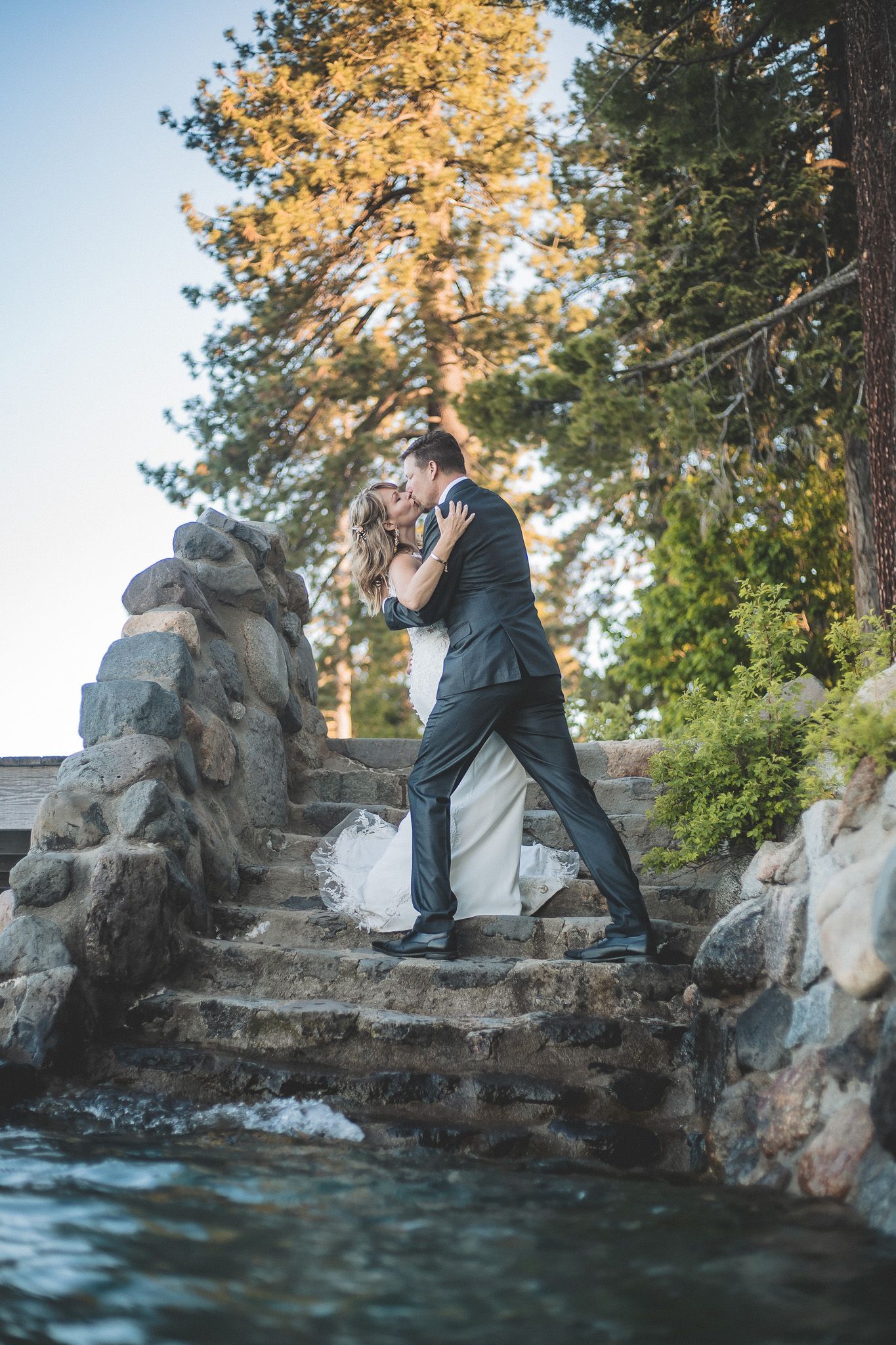 A romantic couple shares an intimate moment on rocky cliffs overlooking a serene lake at sunset.