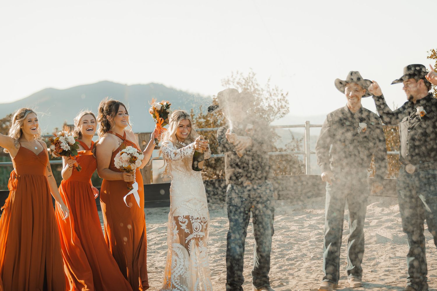 Wedding party celebrates with champagne spray against mountain backdrop.