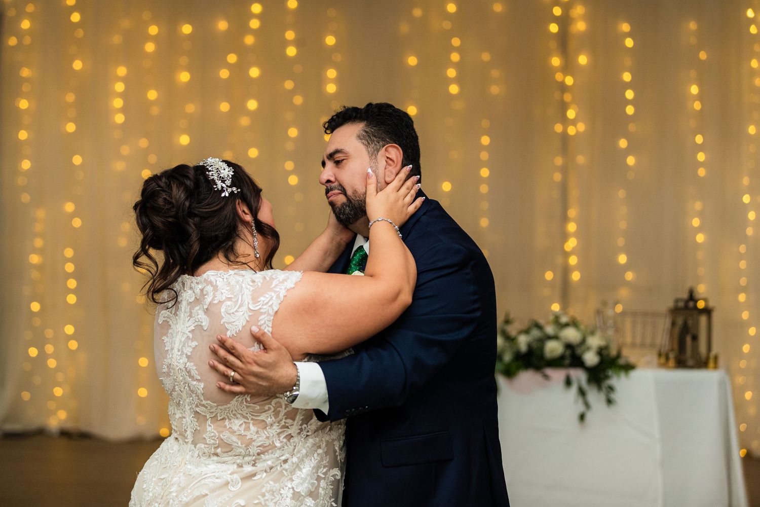 Bride and groom share their first dance in front of a sparkling fairy light backdrop at their wedding reception.