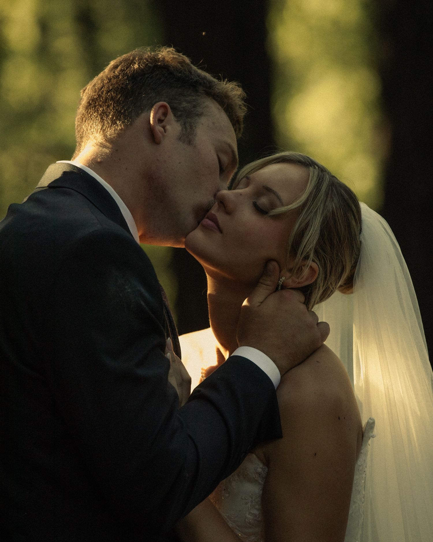 A groom tenderly holds his bride's face for a romantic kiss, her veil softly framing the intimate wedding moment.