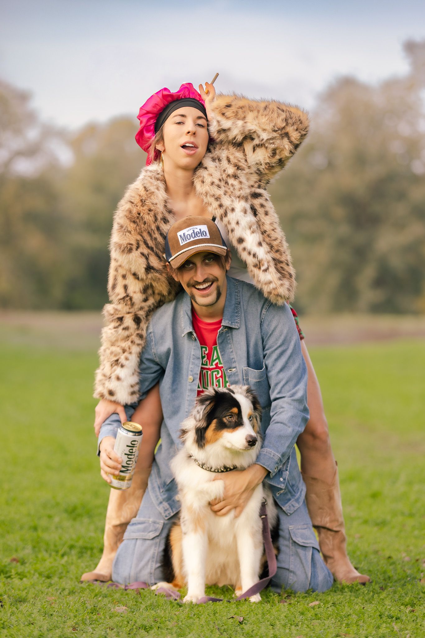 A person in denim and their Australian Shepherd dog sit together on green grass in a field.