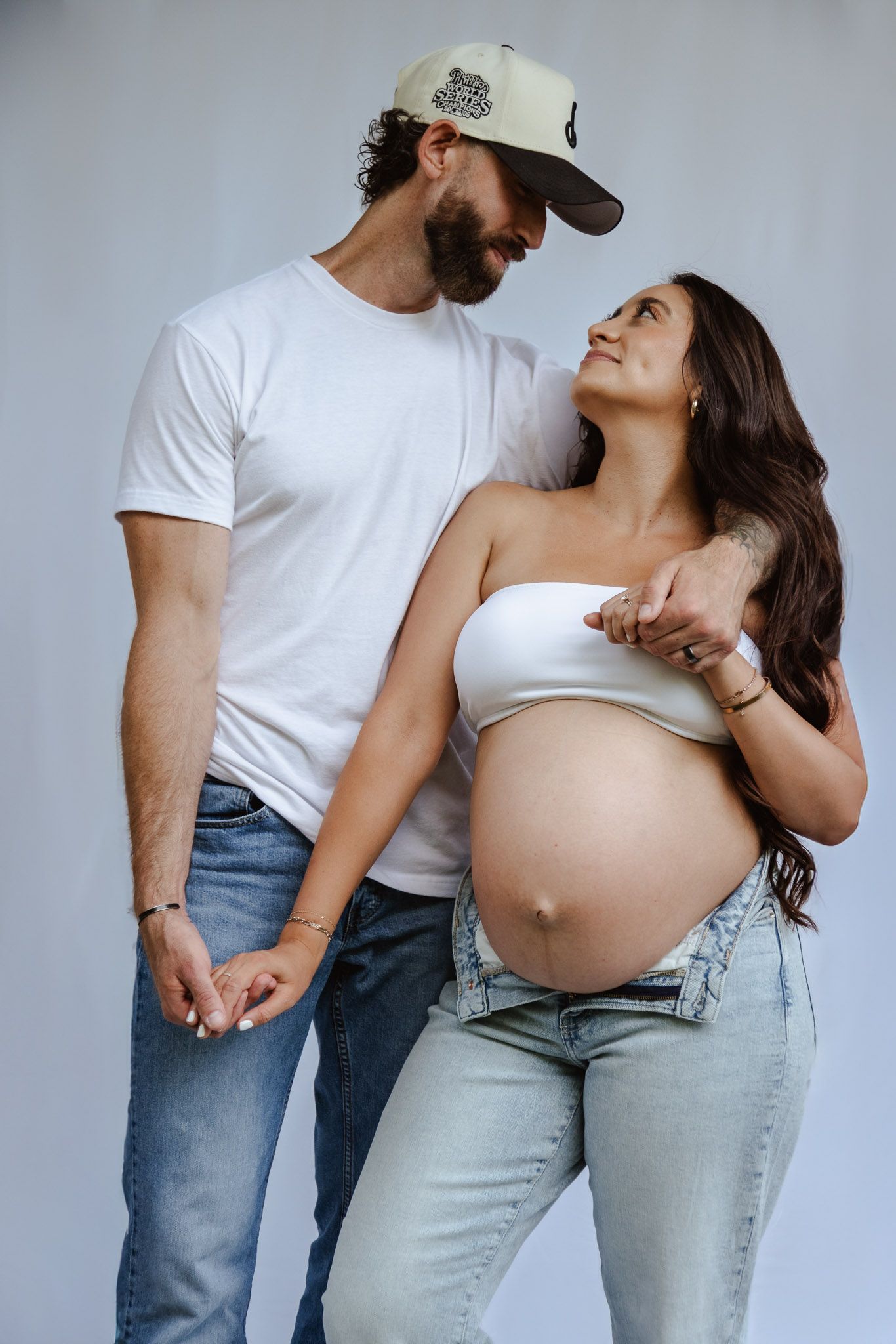 Intimate maternity studio portrait of couple in casual wear against grey background.