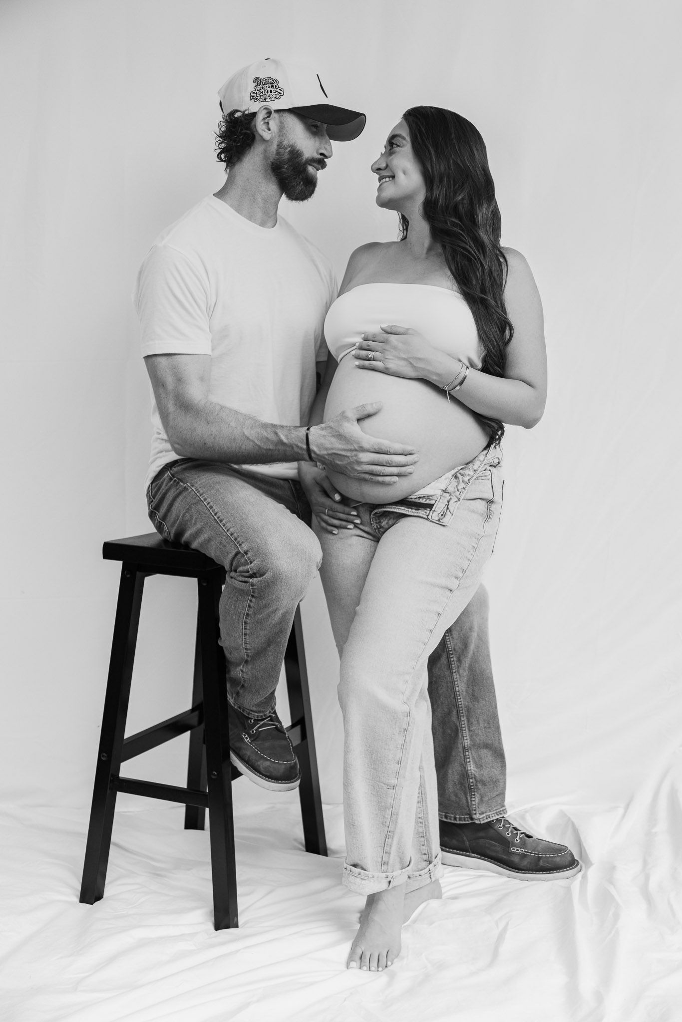 Black and white artistic maternity photo series showing intimate moments between expectant parents in minimalist setting.