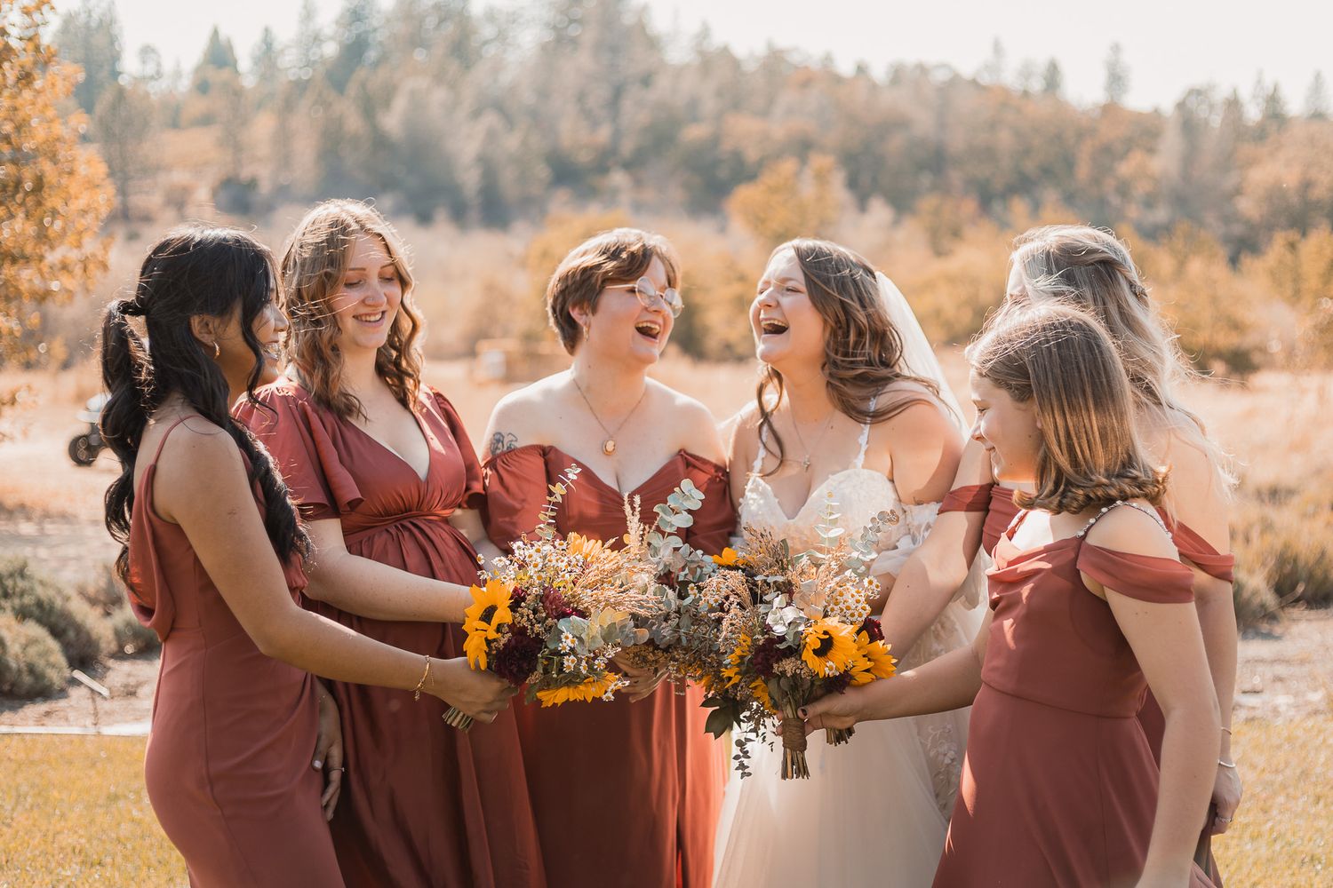 Bridesmaids in burgundy dresses celebrating outdoors with sunflower bouquets.