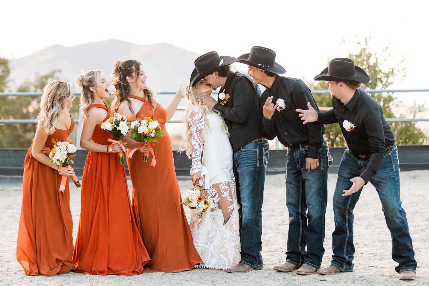 Wedding party in rustic country style with bridesmaids in burnt orange dresses and groomsmen in cowboy attire.