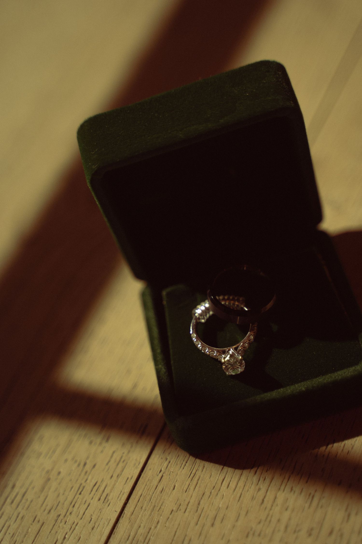 Diamond engagement ring in a dark green velvet box on a wooden surface.