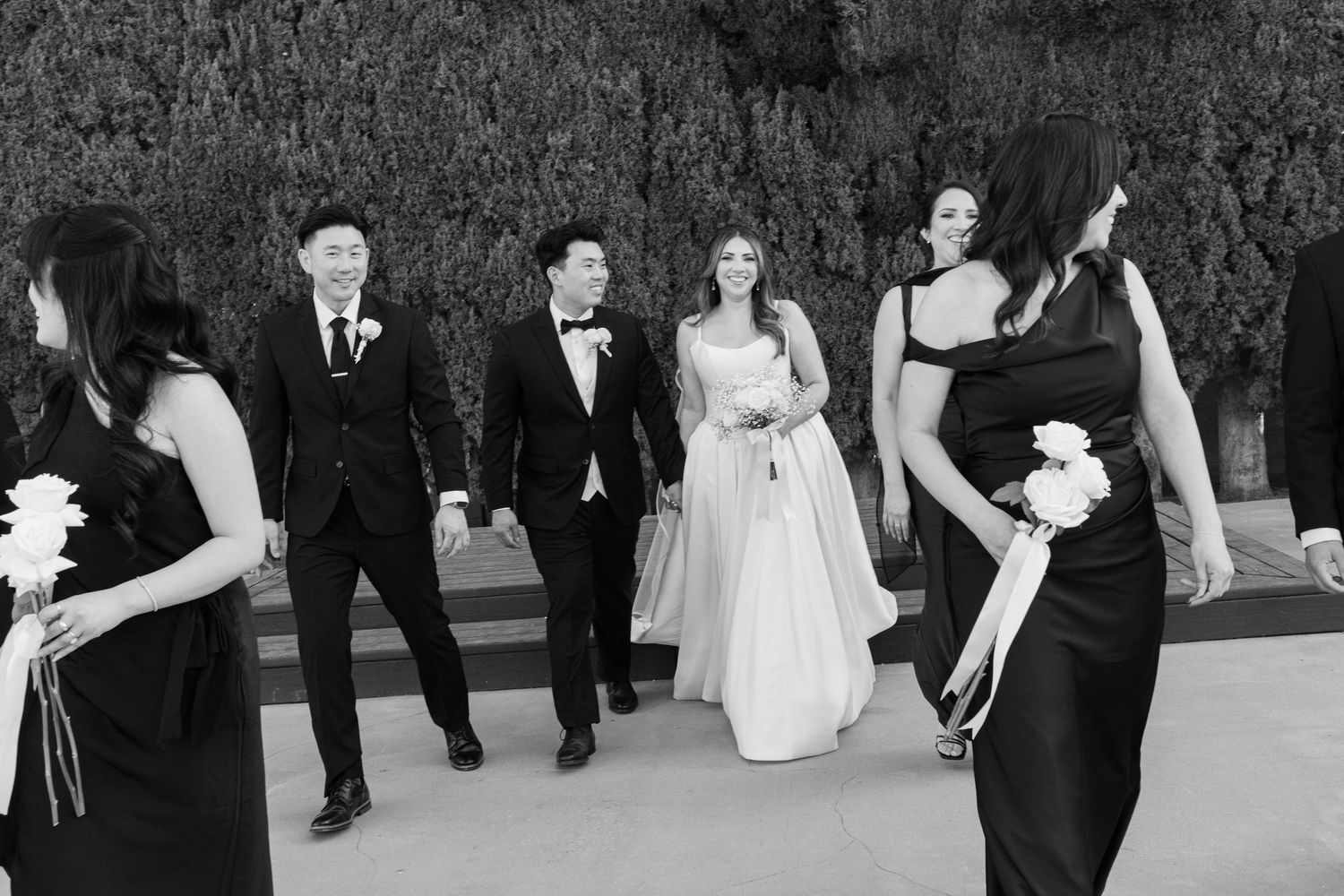 Wedding party walking outdoors in black and white, bride in white gown with groom and bridesmaids in black dresses.