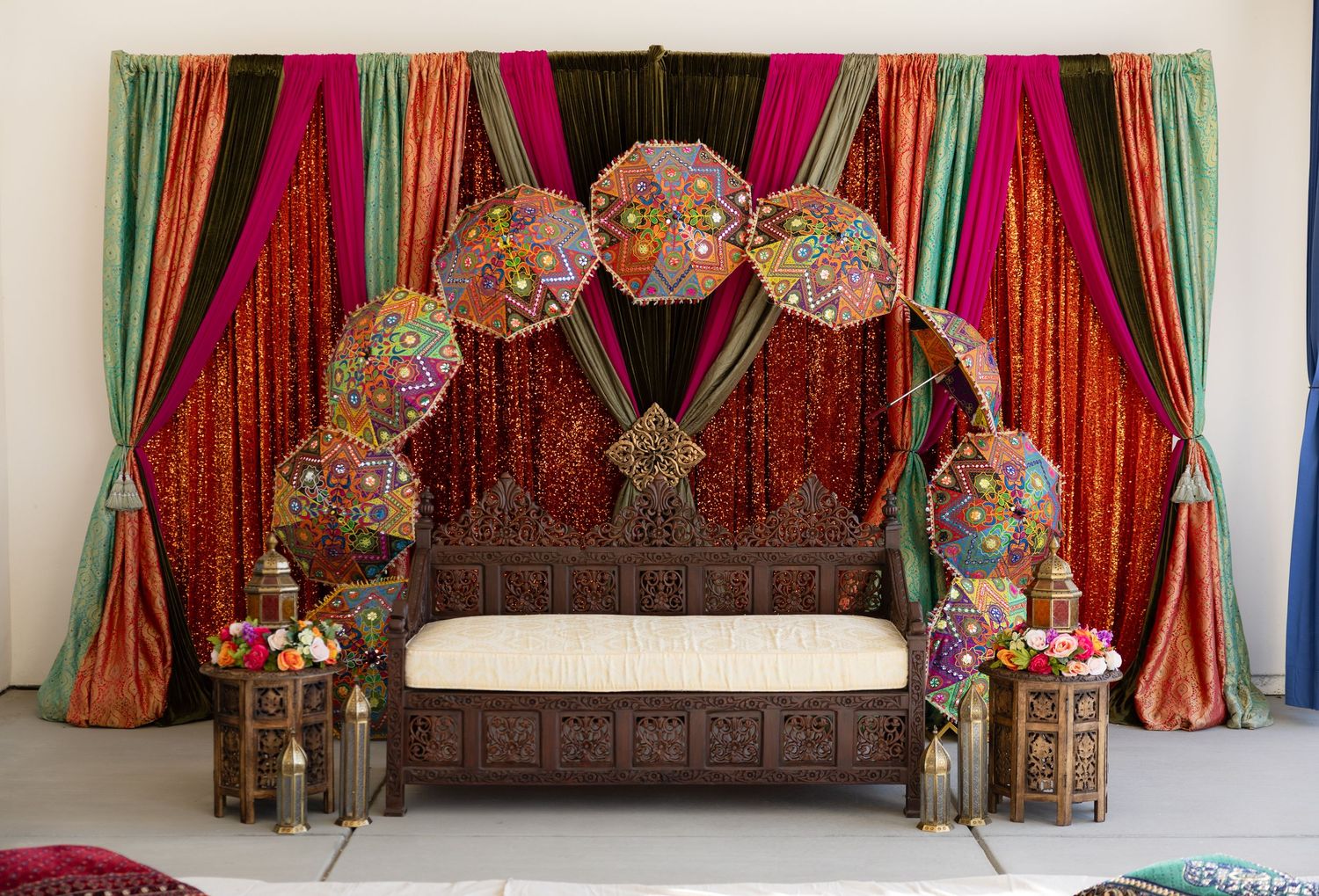 Colorful Indian wedding backdrop with red and gold drapes and hanging decorative elements.