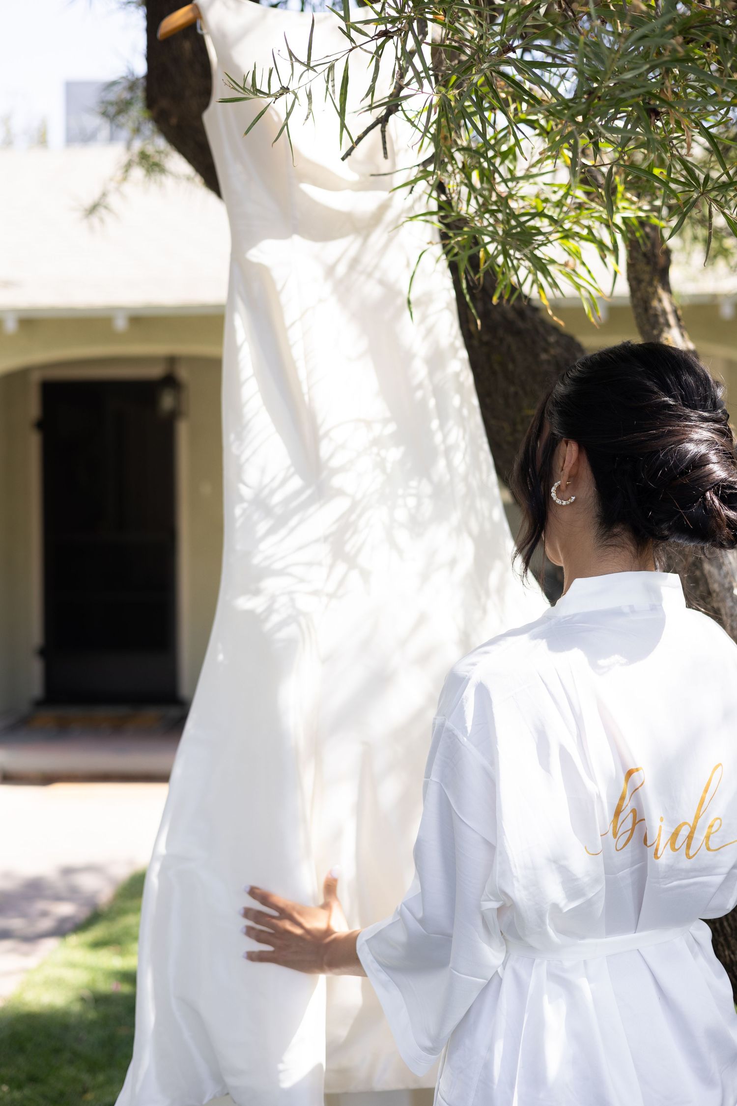 Wedding preparation moment with white robes in sunlit outdoor setting.