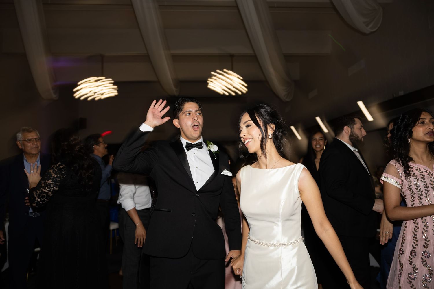 Wedding celebration with people dancing under decorative ceiling lights.