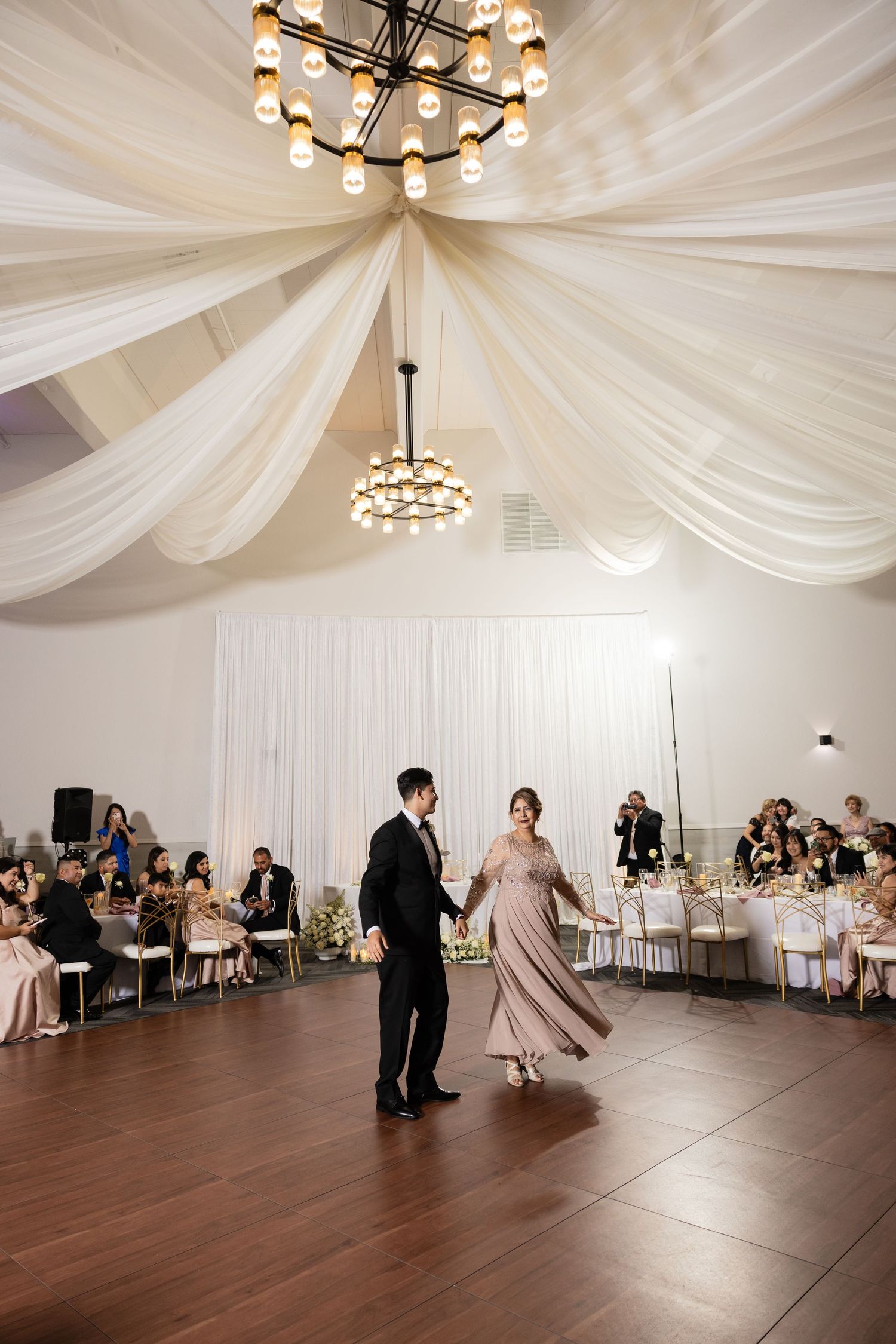 Couples dancing on wooden floor under elegant draped ceiling at wedding reception.