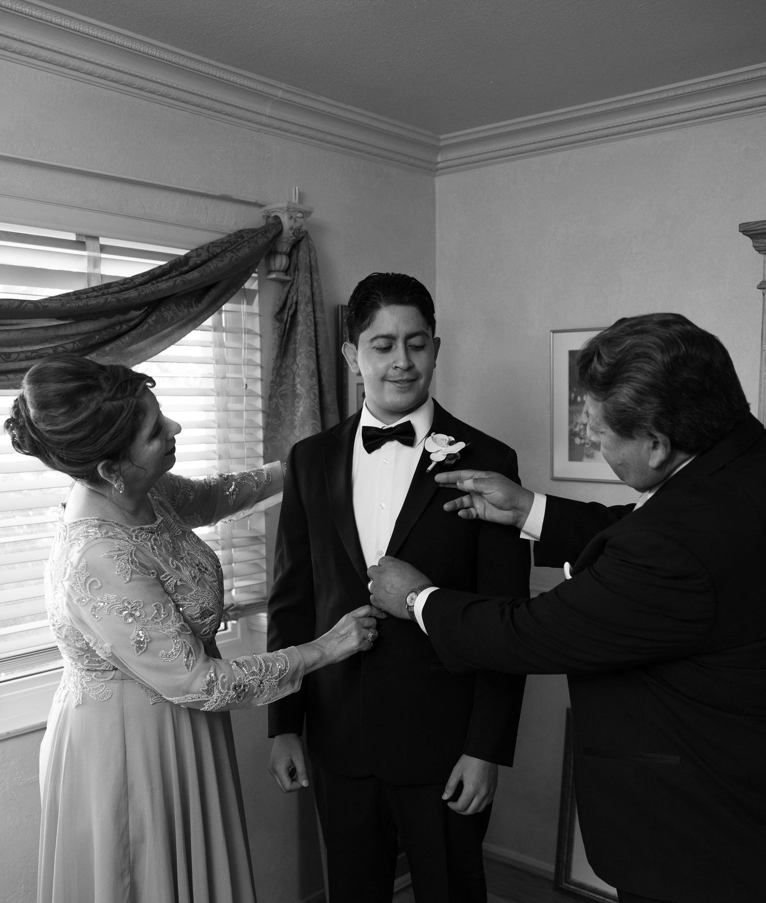 Wedding party members helping adjust formal attire in a bright indoor setting.
