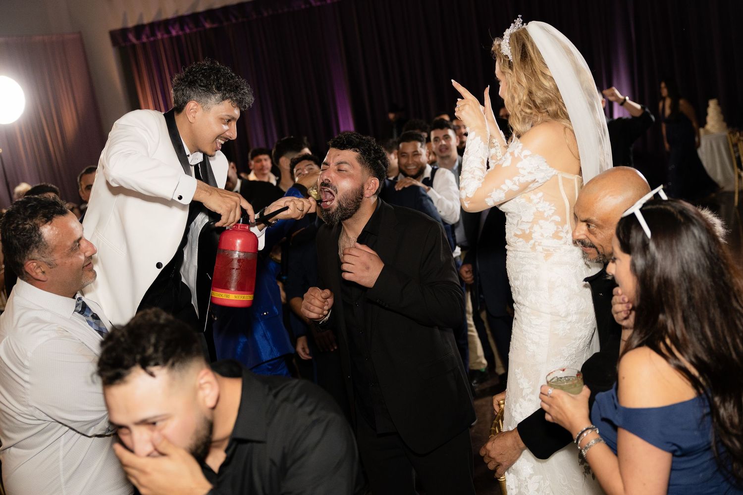 Wedding reception guests celebrate energetically on a crowded dance floor.