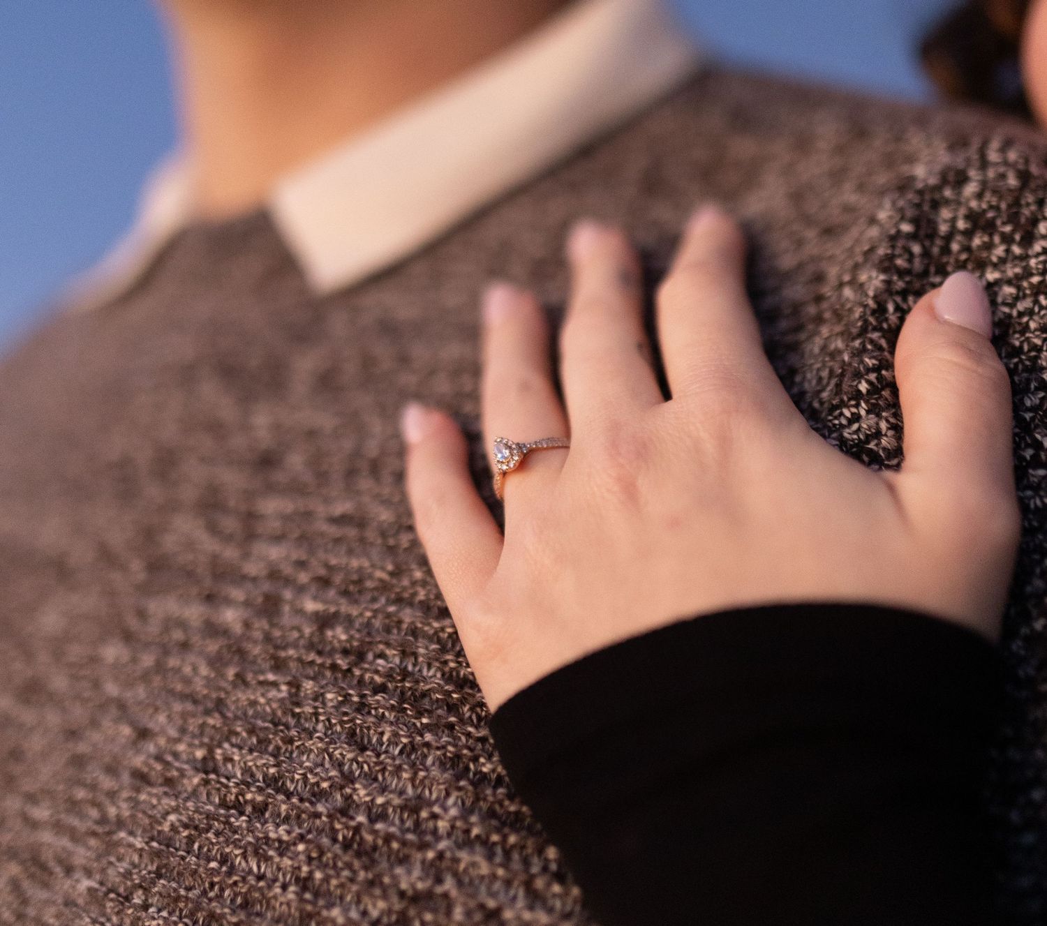Close-up of hand with engagement ring resting on brown knit sweater.