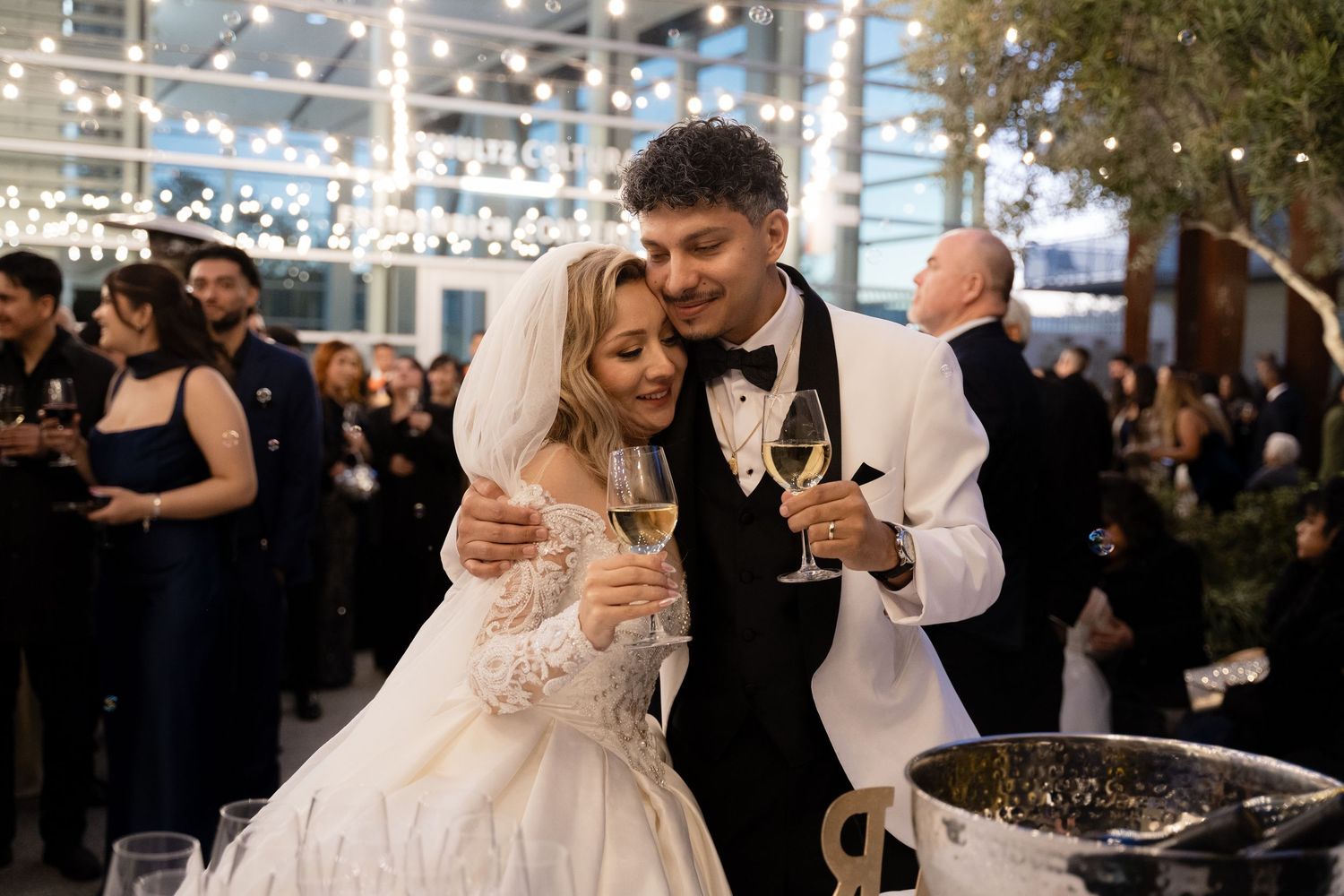Guests gather at a modern wedding reception space with string lights overhead.
