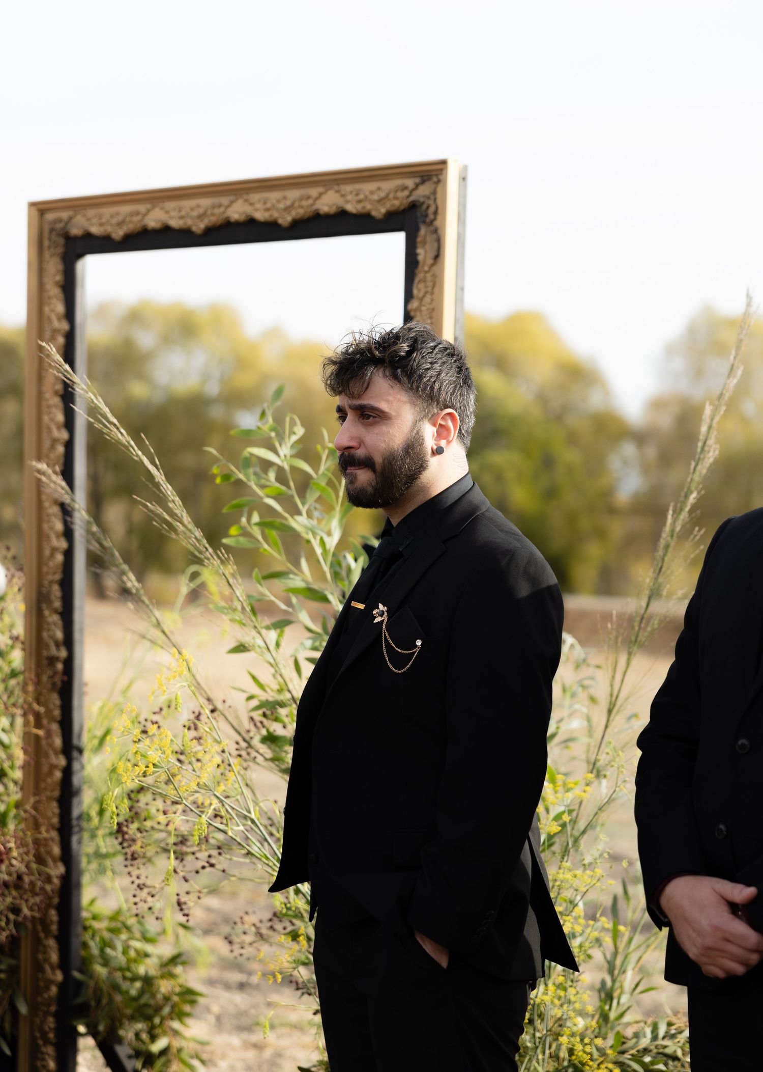 Groomsmen standing in black suits against a rustic wooden frame backdrop.