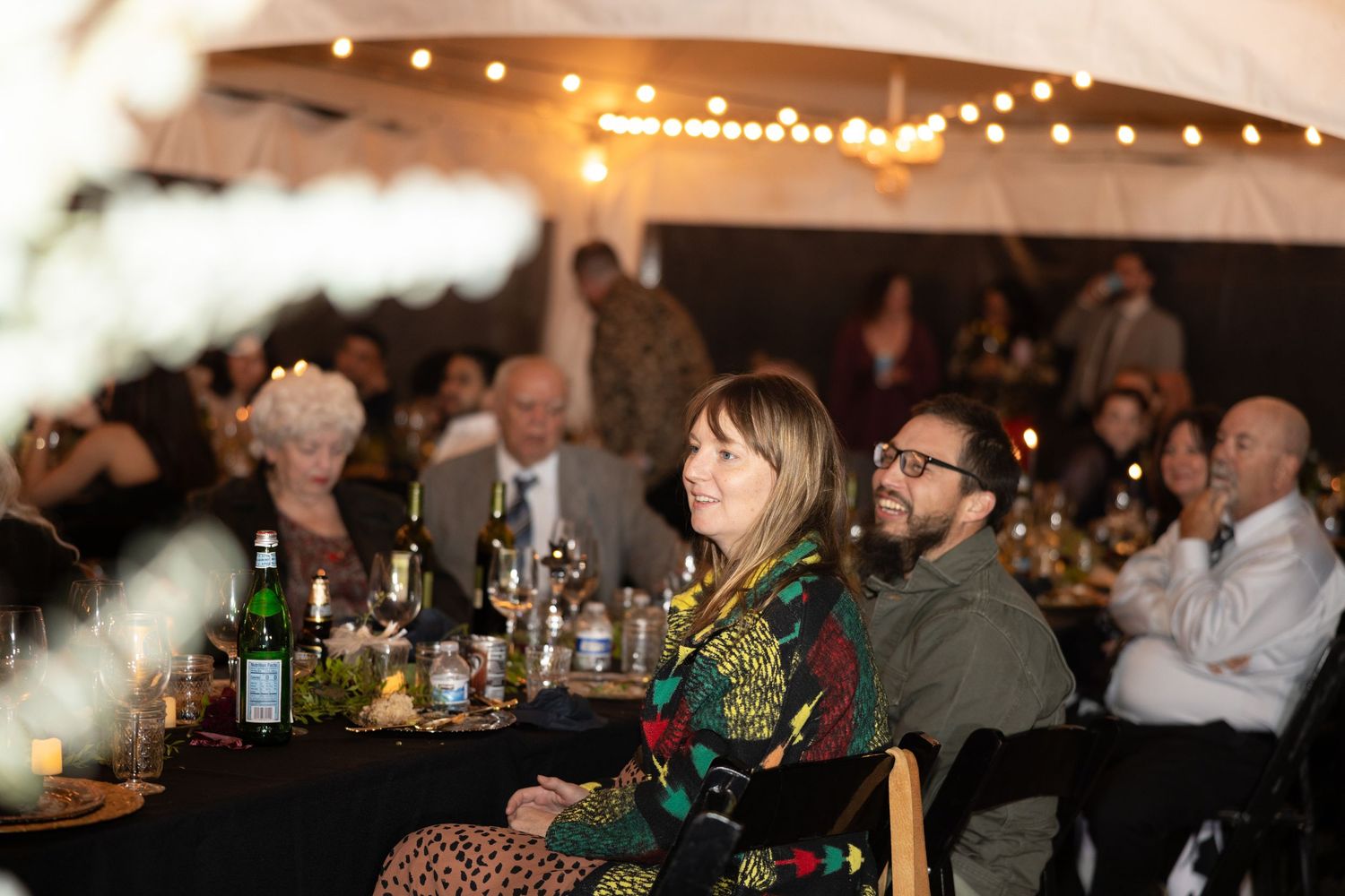 Evening celebration under string lights with guests seated at decorated dining tables.