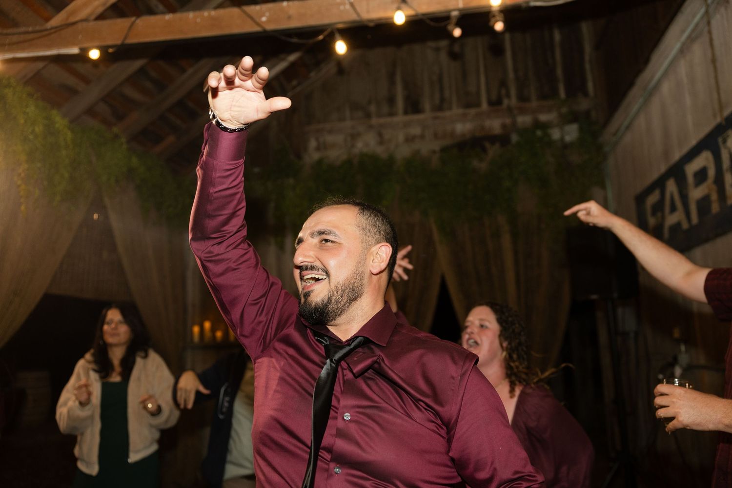 Joyful celebration with dancing guests under string lights at a rustic barn wedding reception.