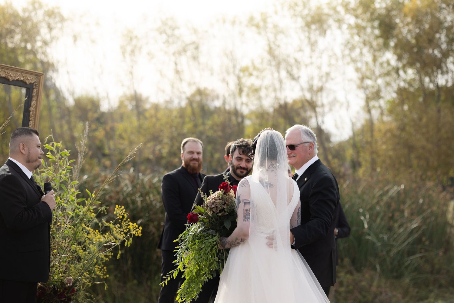 Wedding party members arranged in a curved line during an autumn outdoor ceremony.
