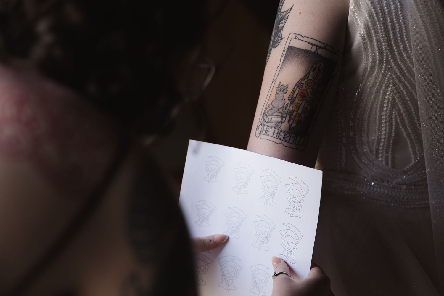 Person sketching a design while showing their tattooed arm.