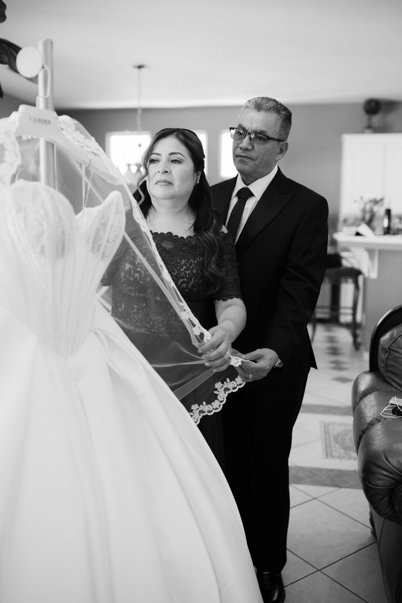 Black and white photo of a bride and older man examining a wedding dress and veil indoors.