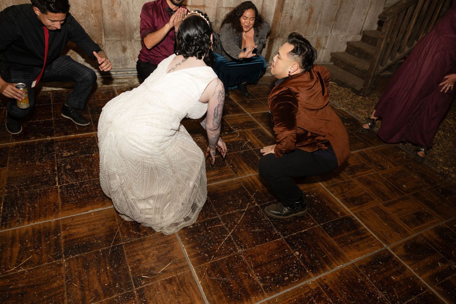 Wedding celebration with dancers on a wooden floor in a rustic barn setting.
