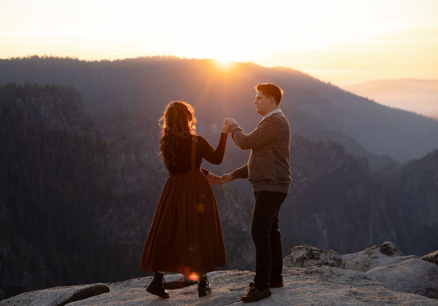 Two people share a romantic dance on a mountain cliff at sunset.
