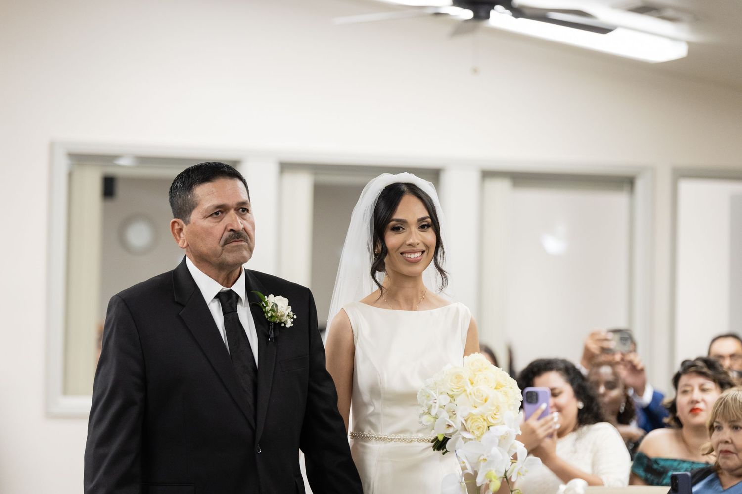 Wedding ceremony processional showing bride and escort walking down church aisle.