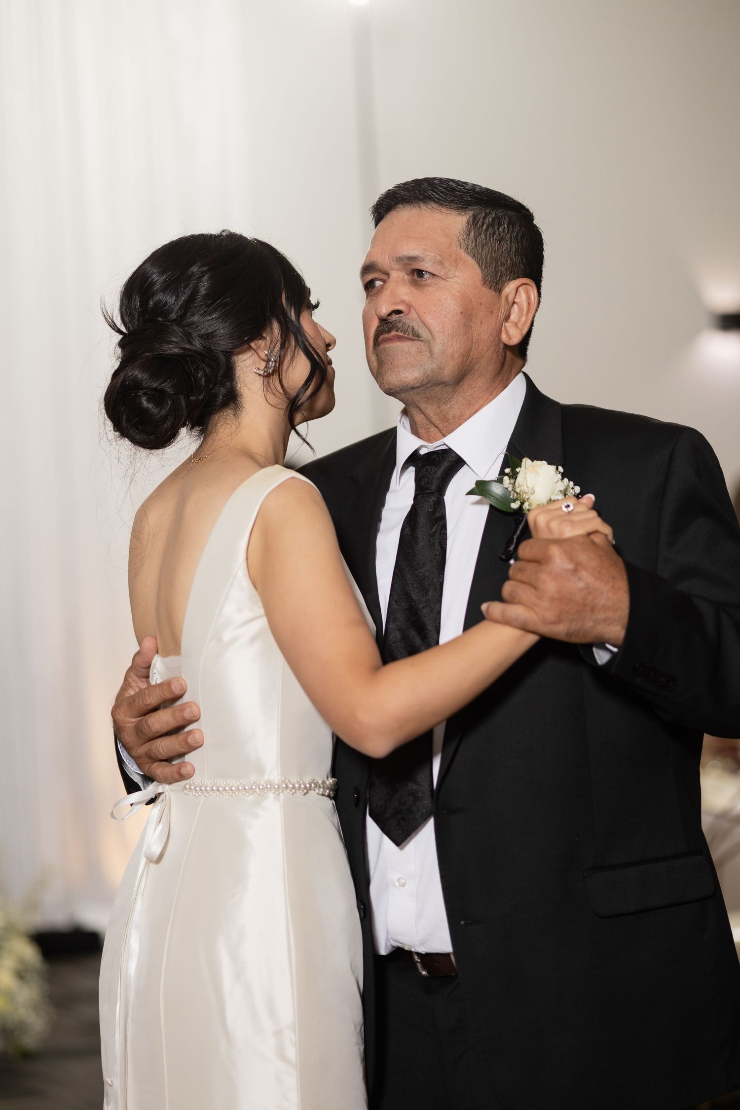 A couple shares an intimate dance at a wedding reception, with the bride wearing a white dress and the groom in a black suit.