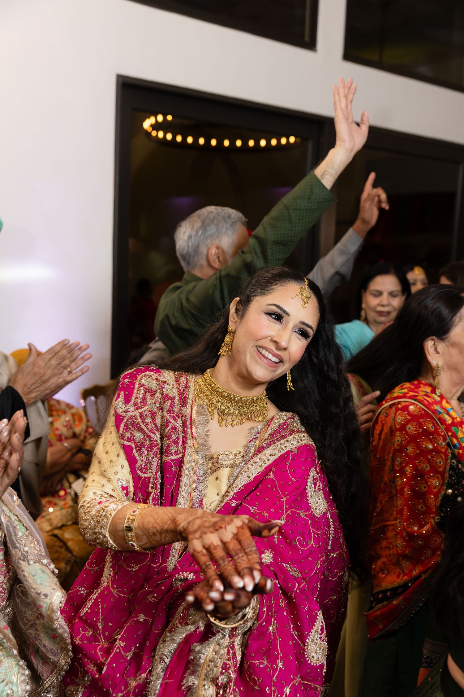 Guests dance and celebrate at an Indian wedding reception wearing vibrant traditional pink and gold attire.