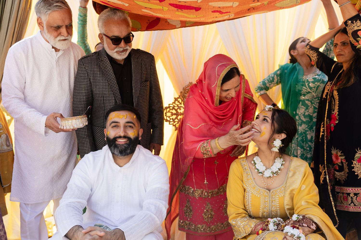 People gathered at a traditional Indian ceremony with participants wearing colorful traditional attire including yellow and red garments.