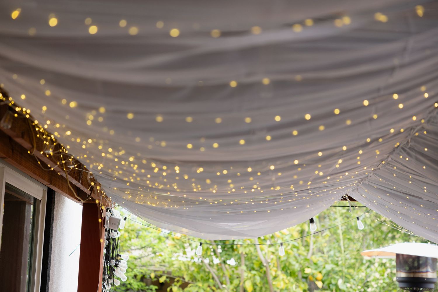 White fabric draping and twinkle lights create an elegant ceiling canopy for an indoor-outdoor event space.