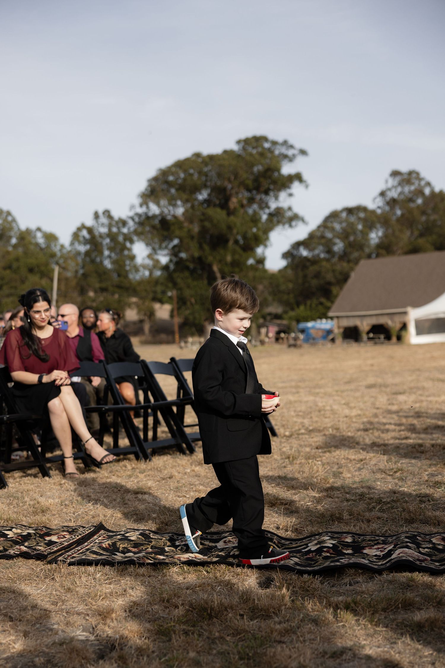 Young attendee sitting on ground during outdoor wedding ceremony.