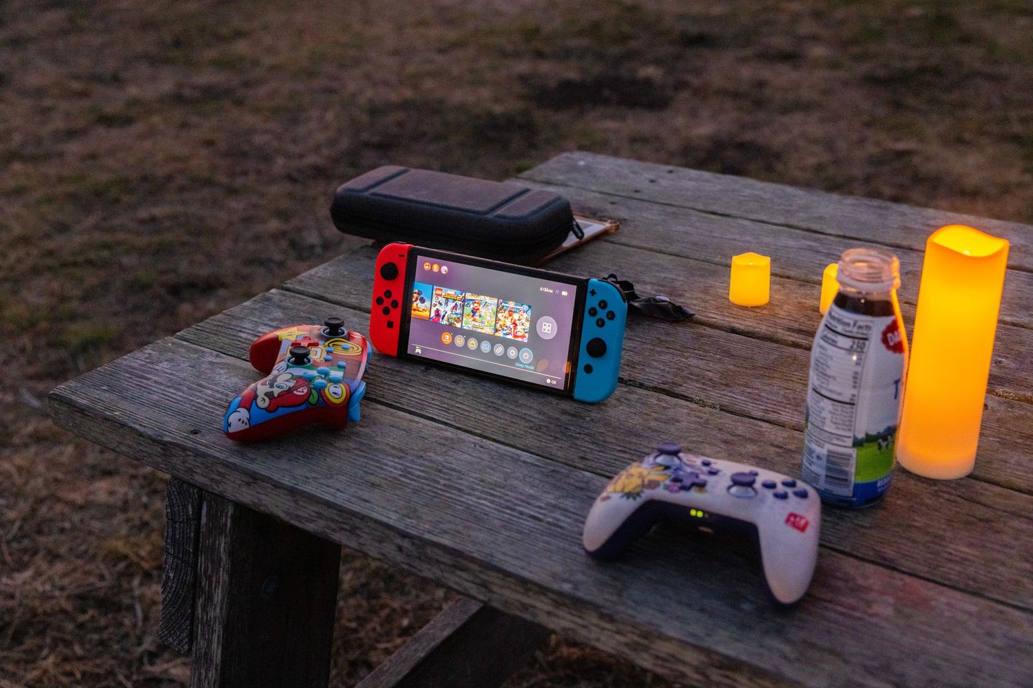 Gaming controllers and candles arranged on wooden outdoor table.