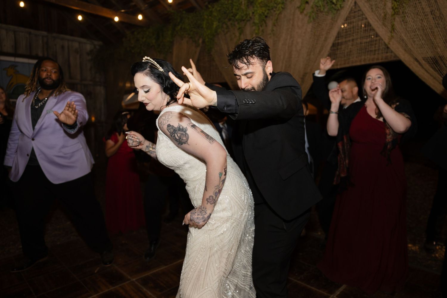 Lively dance floor moments captured during a rustic barn wedding reception with string lighting.