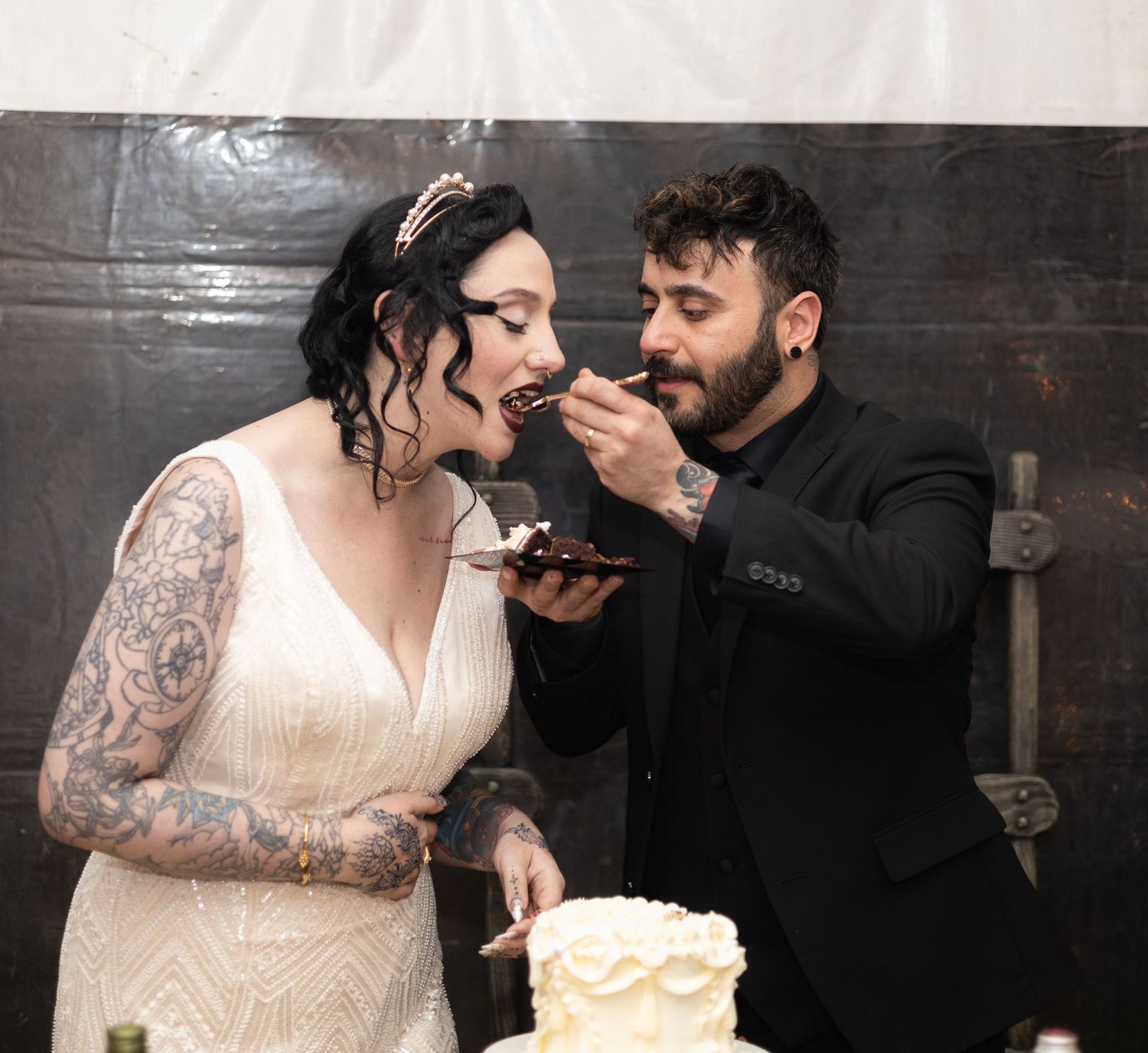 Newlyweds share a playful moment while cutting their wedding cake at a rustic venue.