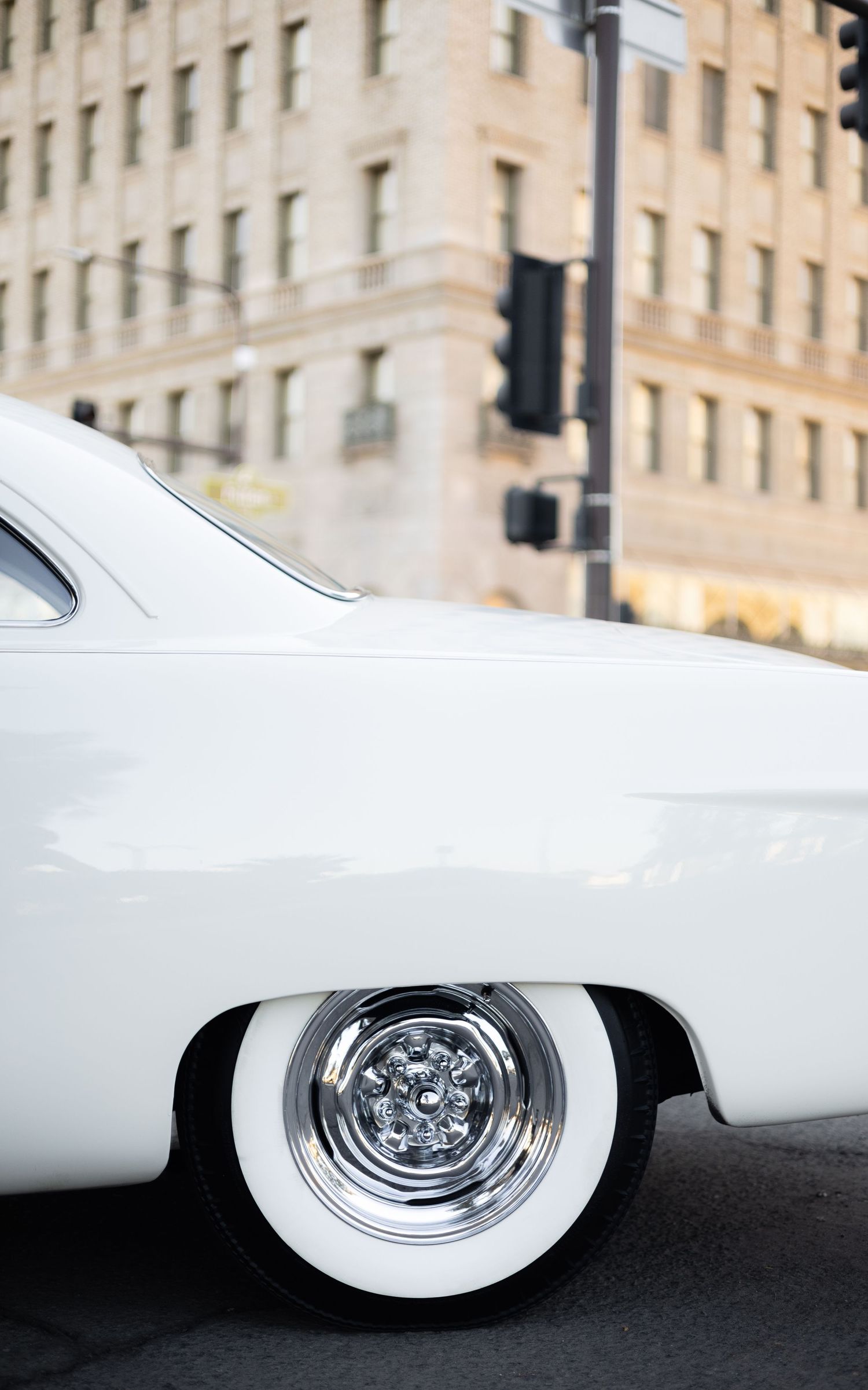 Classic white car with vintage whitewall tires parked in front of historic building.