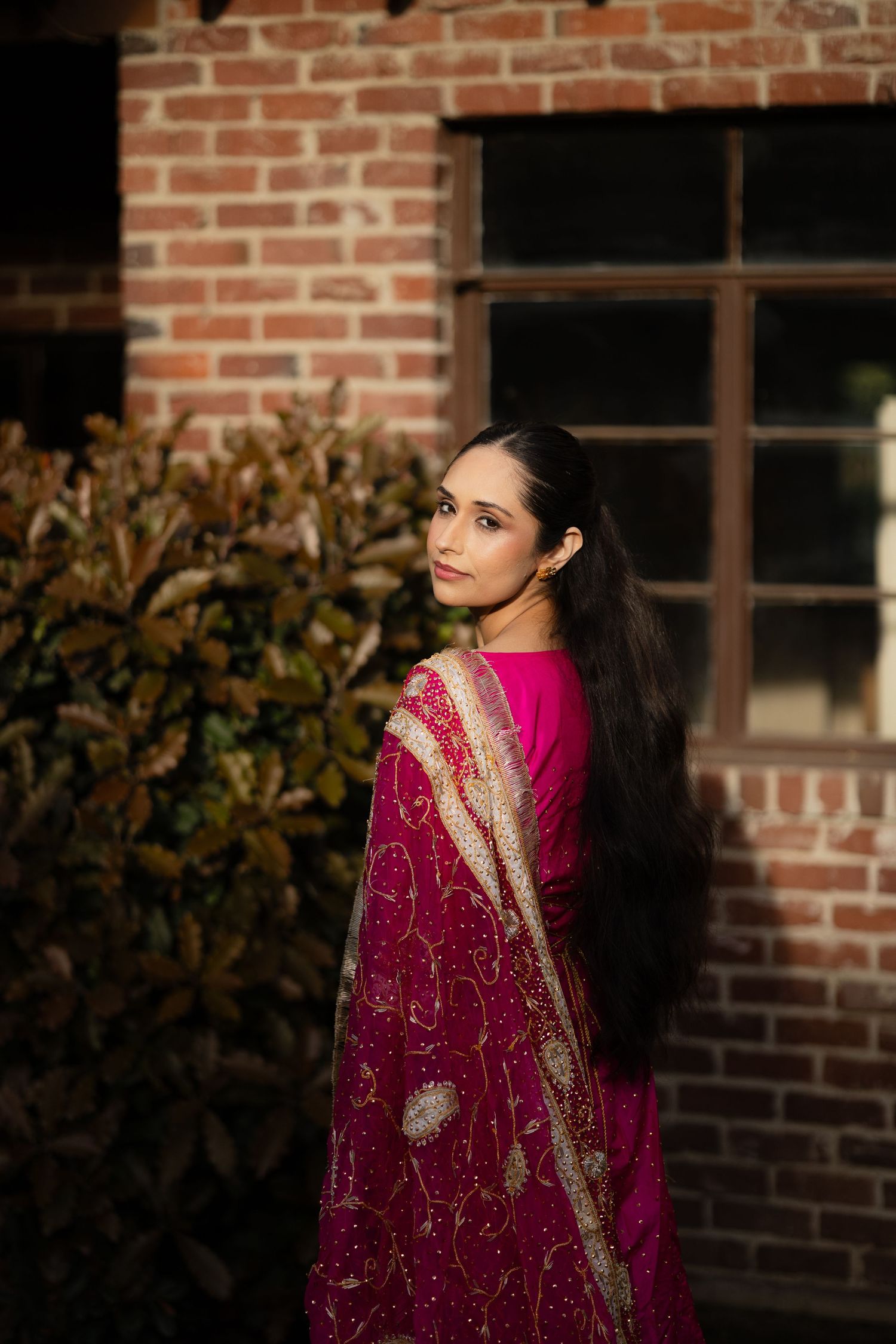Ornate magenta and gold embroidered sari details captured against rustic brick wall backdrop.