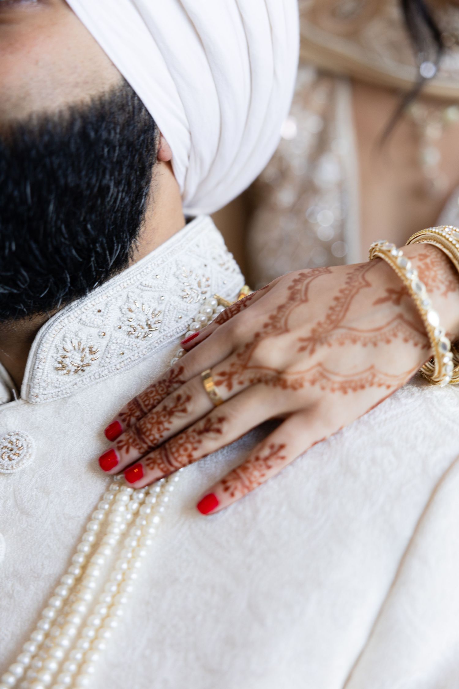 Close-up details of intricate henna designs and pearl jewelry on a bride wearing white.