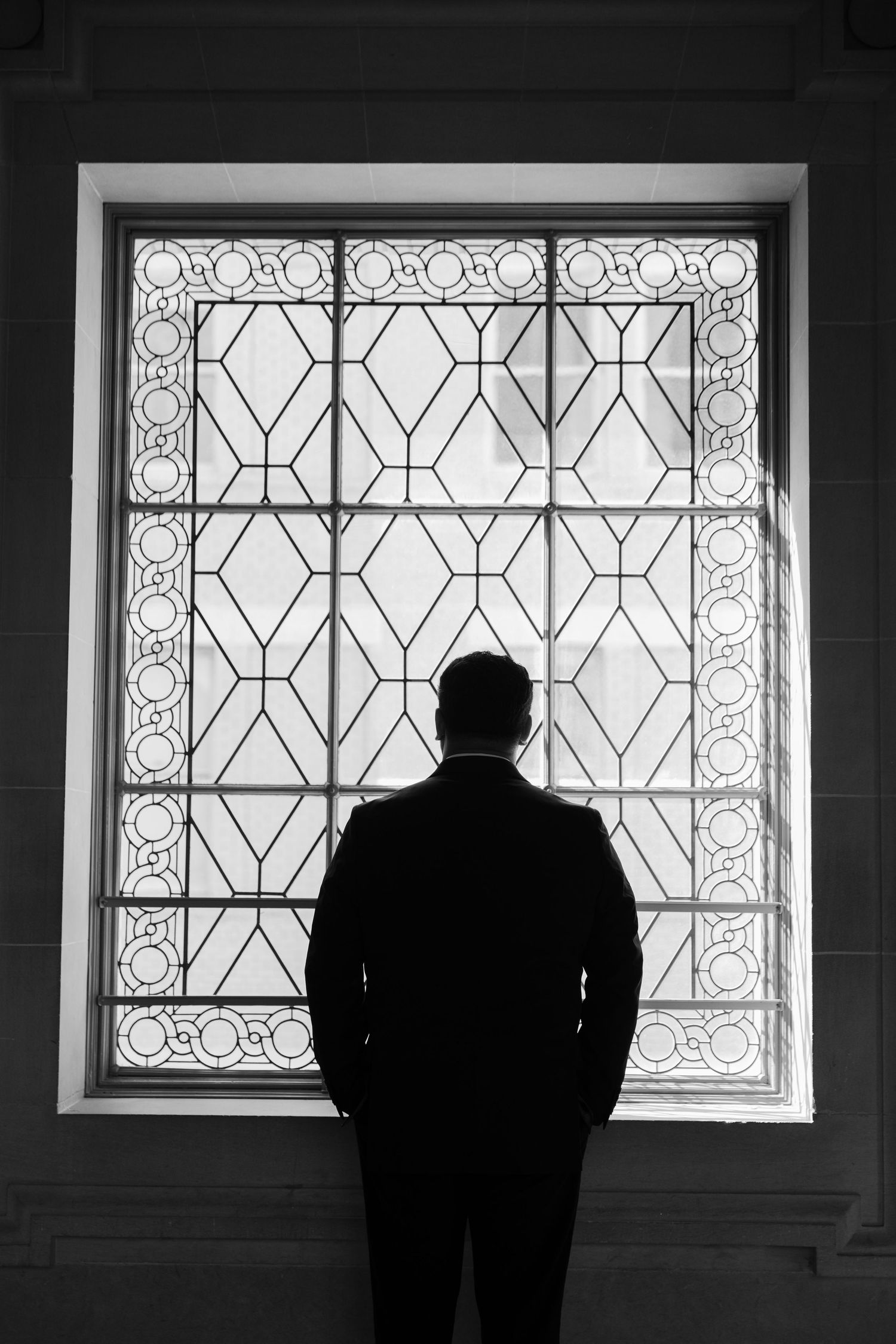 Dark silhouettes standing before ornate art deco windows with geometric patterns.